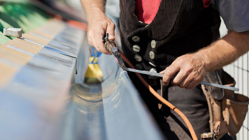 Handwerker repariert Dachrinne beim Dach sanieren im Burgenland